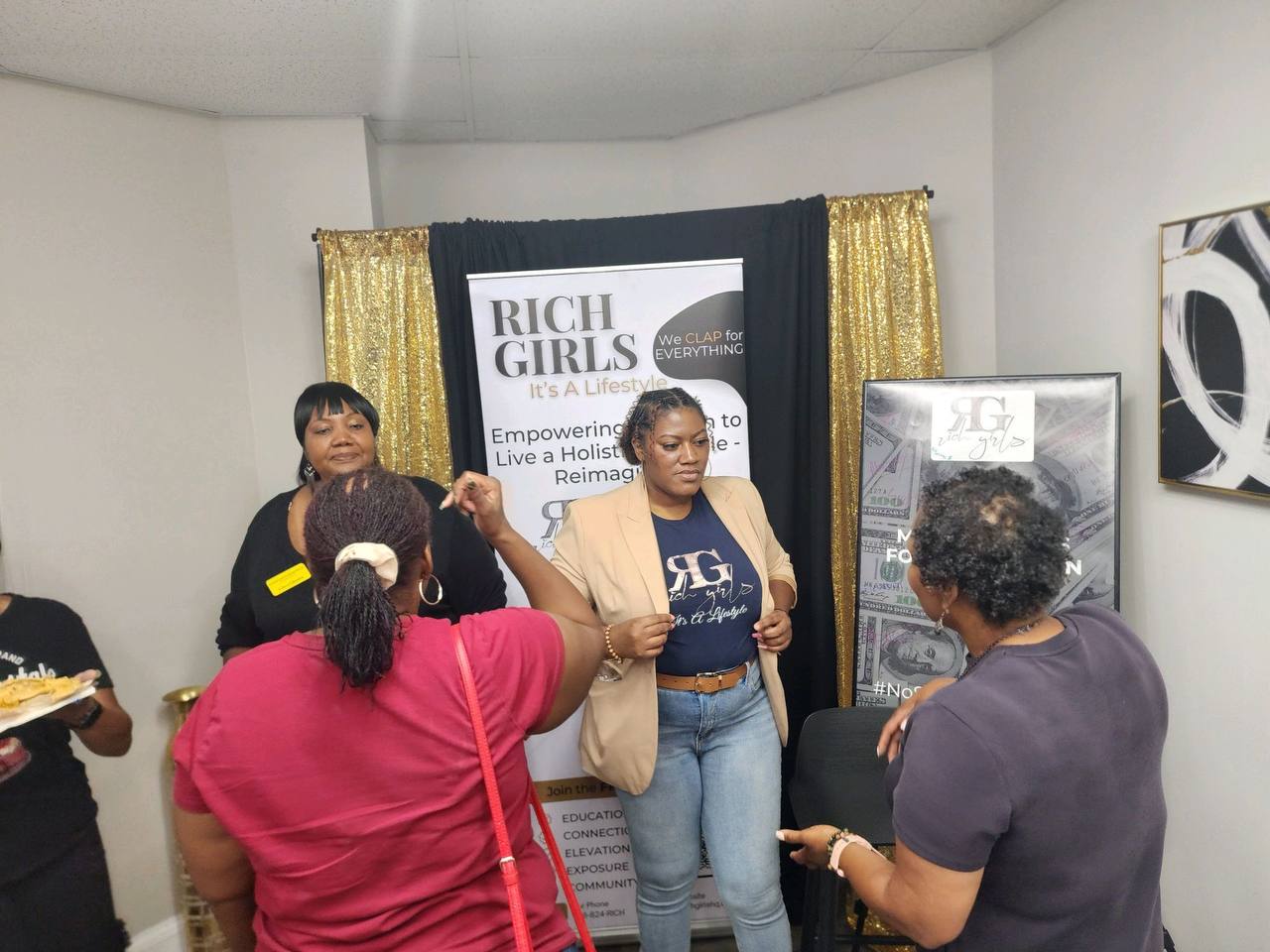 A Rich Girls Foundation facilitator speaking with attendees in front of the Rich Girls banner