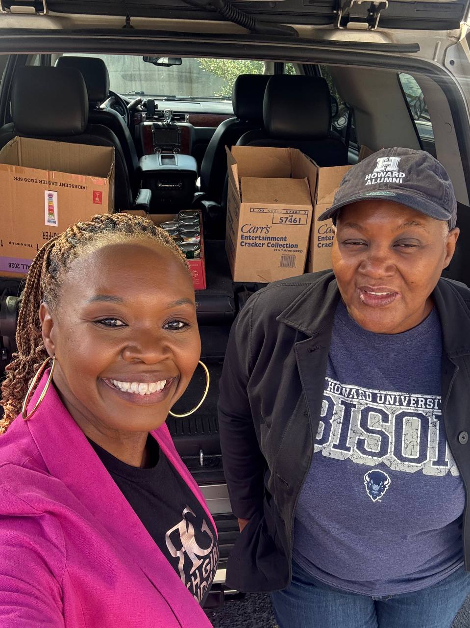Two Rich Girls Foundation volunteers with donation boxes loaded in a vehicle